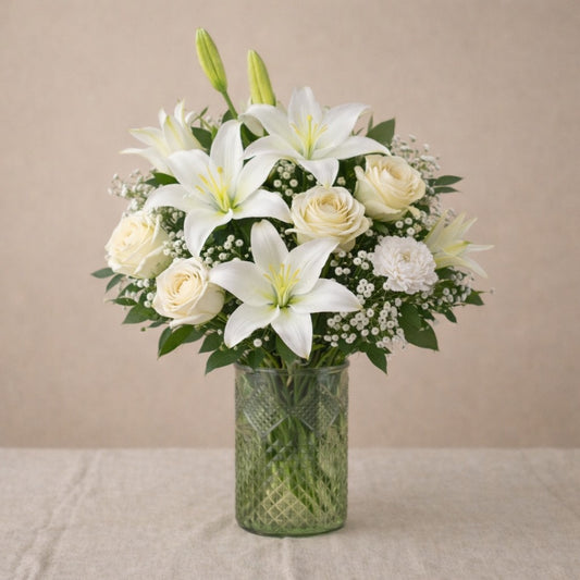 Deluxe size Serenity Grace sympathy flower arrangement with white lilies, ivory roses, chrysanthemums, and fuller greenery arranged in a clear glass vase — Escondido florist.
