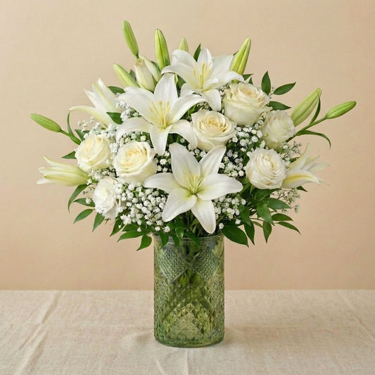 Extra full size Serenity Grace elegant white sympathy arrangement showcasing abundant white lilies, ivory roses, chrysanthemums, and lush greenery in a clear glass vase — Escondido florist.