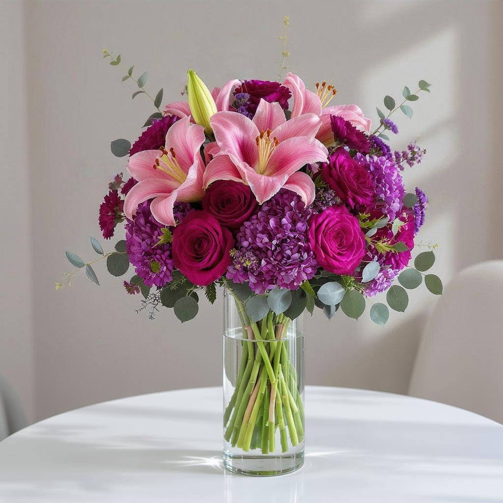 Premium size vibrant pink and purple floral arrangement with lilies, roses, ranunculus, and lush greenery in a clear glass vase — Oceanside flower delivery.