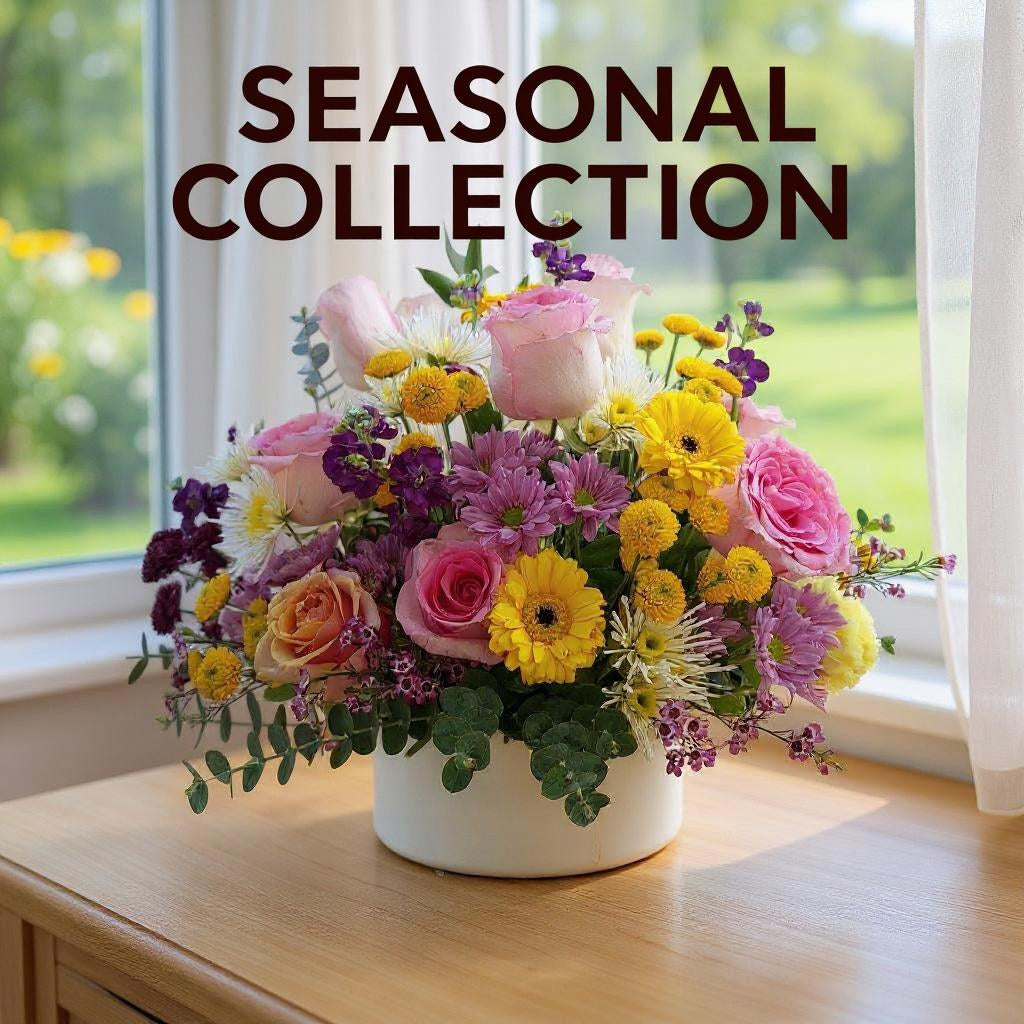 Colorful seasonal flower arrangement with pink roses, yellow gerbera daisies, and mixed blooms in a white vase by a sunlit window — handcrafted and delivered to San Marcos, Vista, Escondido, Oceanside, and Carlsbad.