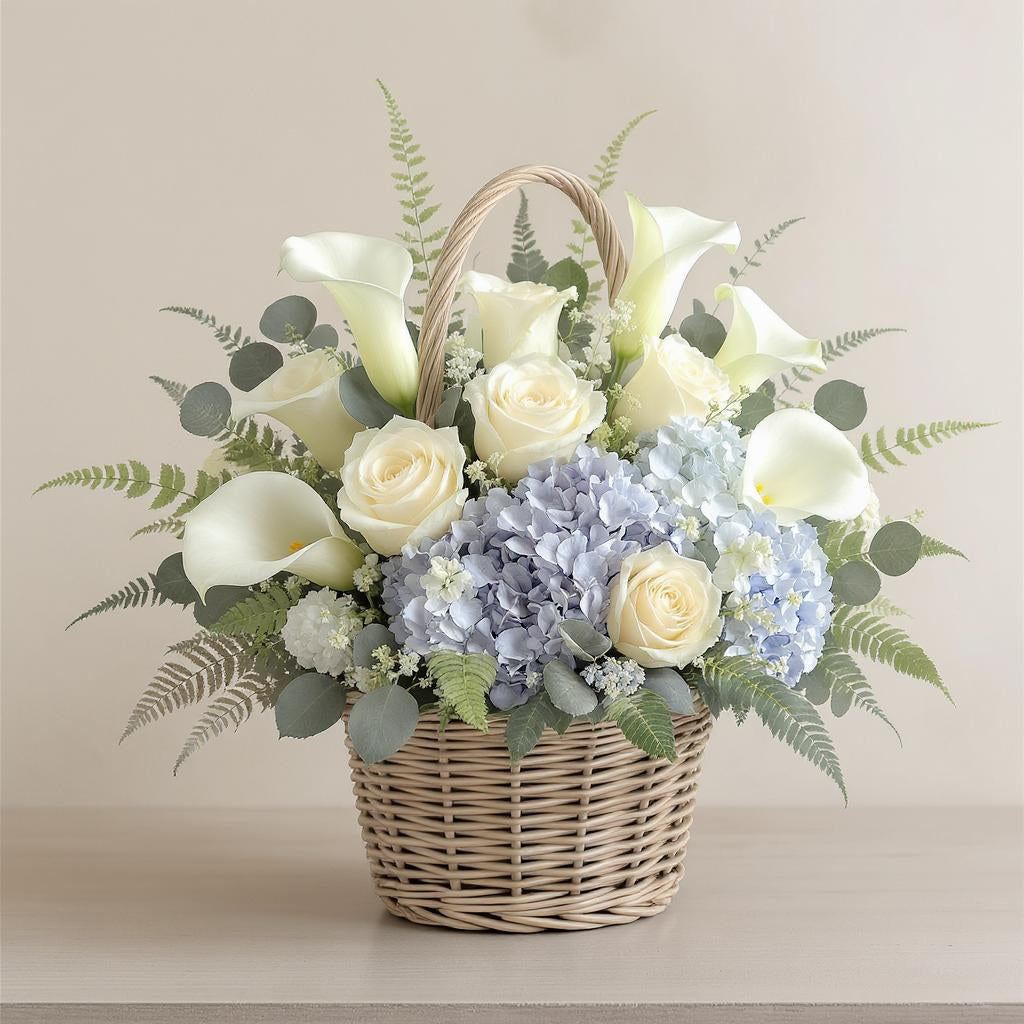Deluxe size rose, calla lily, and hydrangea basket with fuller cream roses, additional calla lilies, enriched blue hydrangeas, and lush greenery in a woven wicker basket — Oceanside florist.