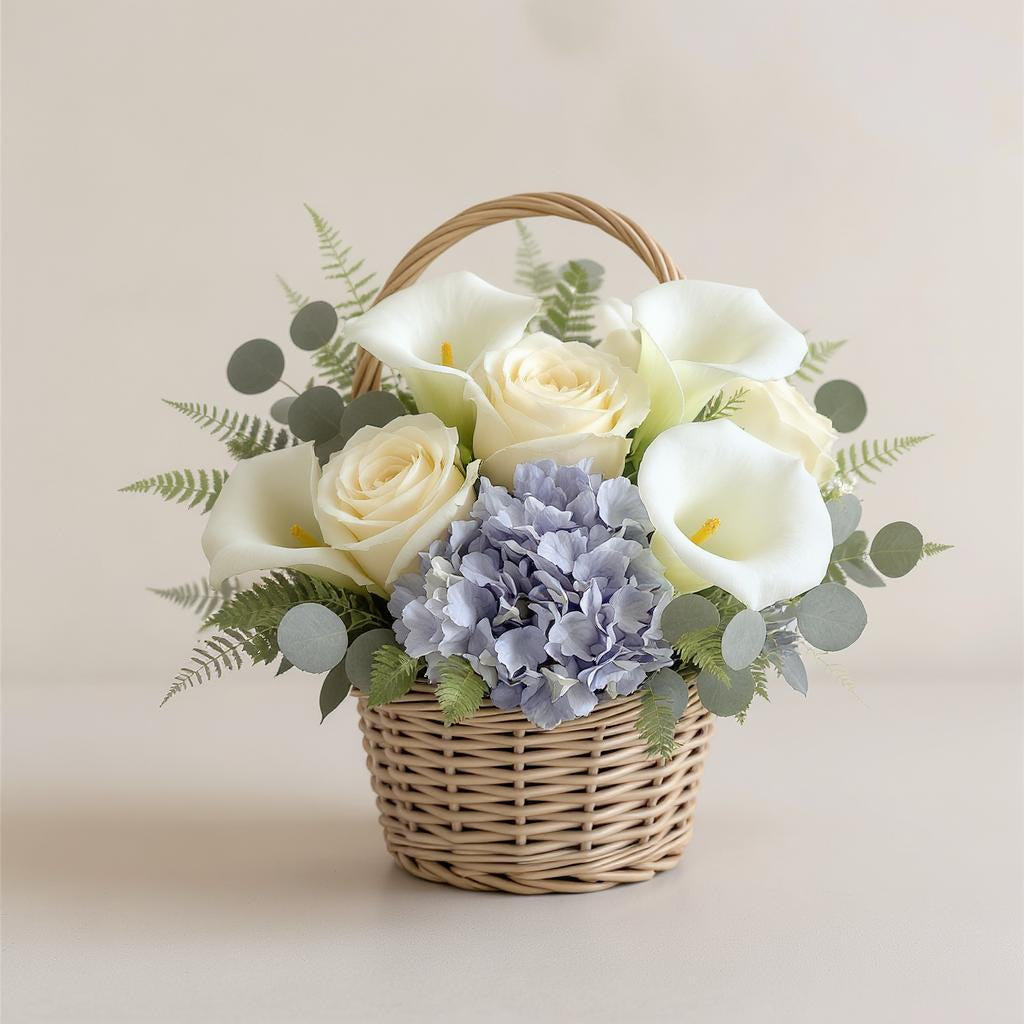 Regular size elegant flower basket featuring cream roses, white calla lilies, blue hydrangeas, and soft greenery arranged in a woven wicker basket — Oceanside florist.