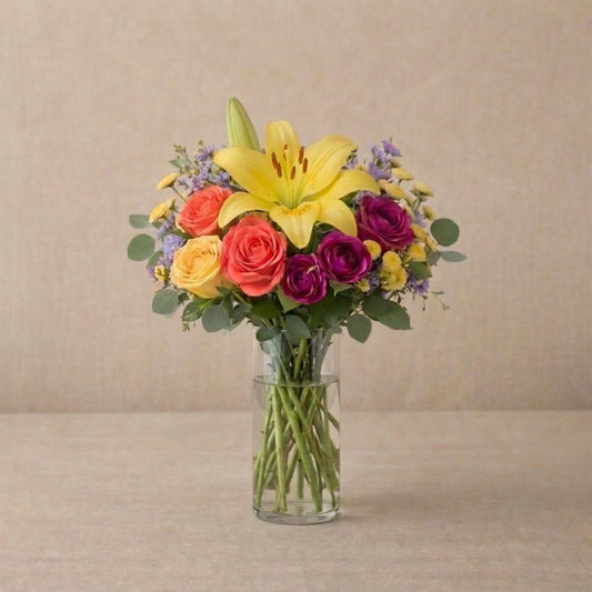Regular size Amber Celebration yellow lily and orange rose bouquet in clear glass vase with eucalyptus and yellow button blooms – San Marcos flower delivery
