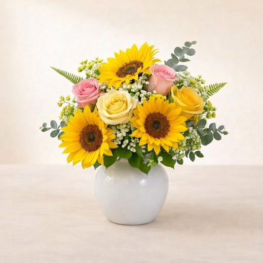 Regular size birthday bouquet featuring bright sunflowers, pink roses, white button mums, and fresh greenery arranged in a white ceramic vase – Vista florist.