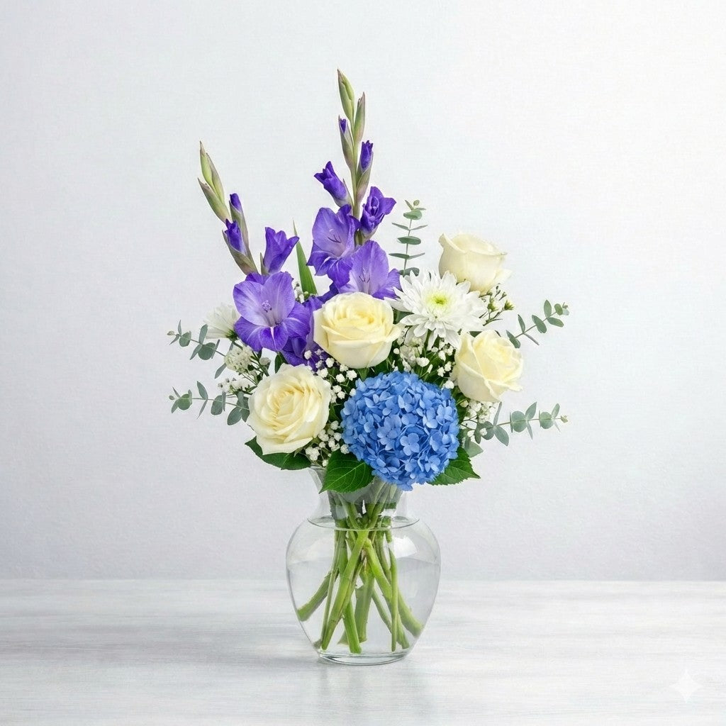 Blue and white serenity vase arrangement with blue hydrangea, white roses, purple gladiolus, white mums, baby’s breath, and eucalyptus in a clear glass vase - Encinitas florist.