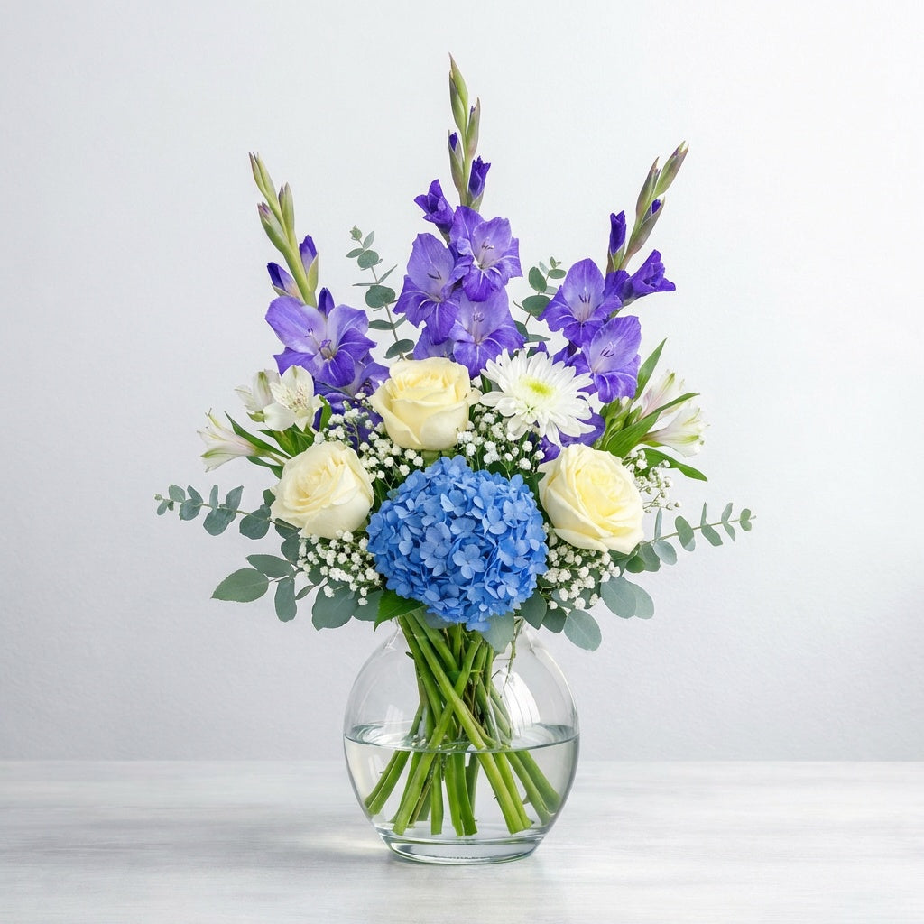 Deluxe blue and white vase arrangement featuring fuller blue hydrangea, white roses, purple gladiolus, white mums, baby’s breath, and eucalyptus greenery - Encinitas florist.