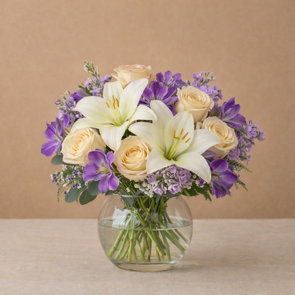 Yellow lily and violet aster bouquet with cream roses arranged in a round glass vase, soft garden style — Same-day flowers Vista.