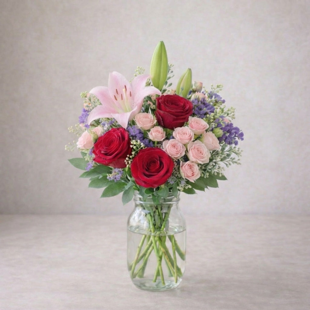 Regular size pink lily and red rose vase arrangement with spray roses, soft lavender fillers, and light greenery in a clear glass vase. Fresh flowers Encinitas CA