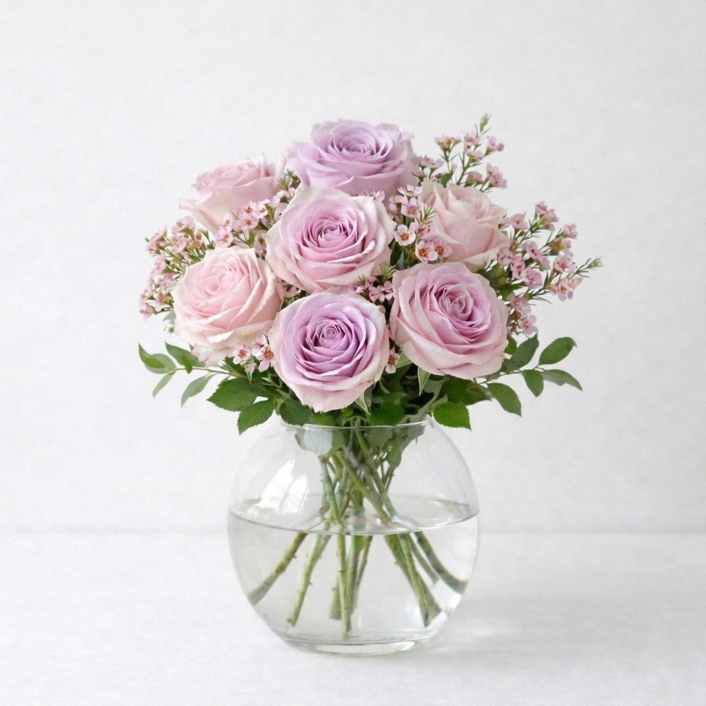 Soft lavender and blush pink rose arrangement with airy spacing and light fillers in a clear round glass vase, designed with natural balance and gentle elegance, fresh flowers Escondido CA.