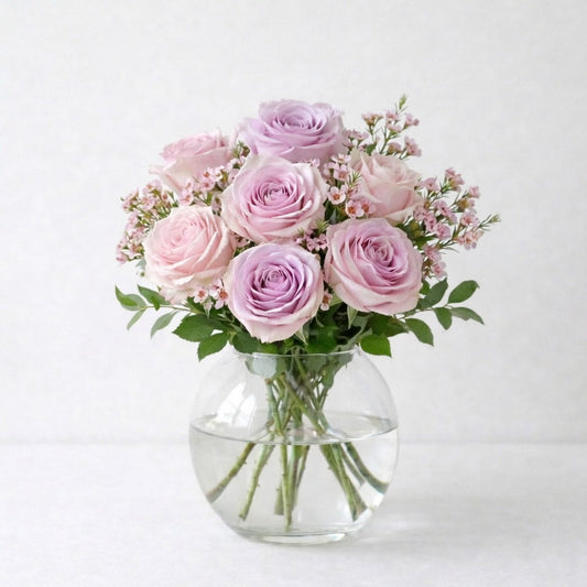 Soft lavender and blush pink rose arrangement with airy spacing and light fillers in a clear round glass vase, designed with natural balance and gentle elegance, fresh flowers Escondido CA.
