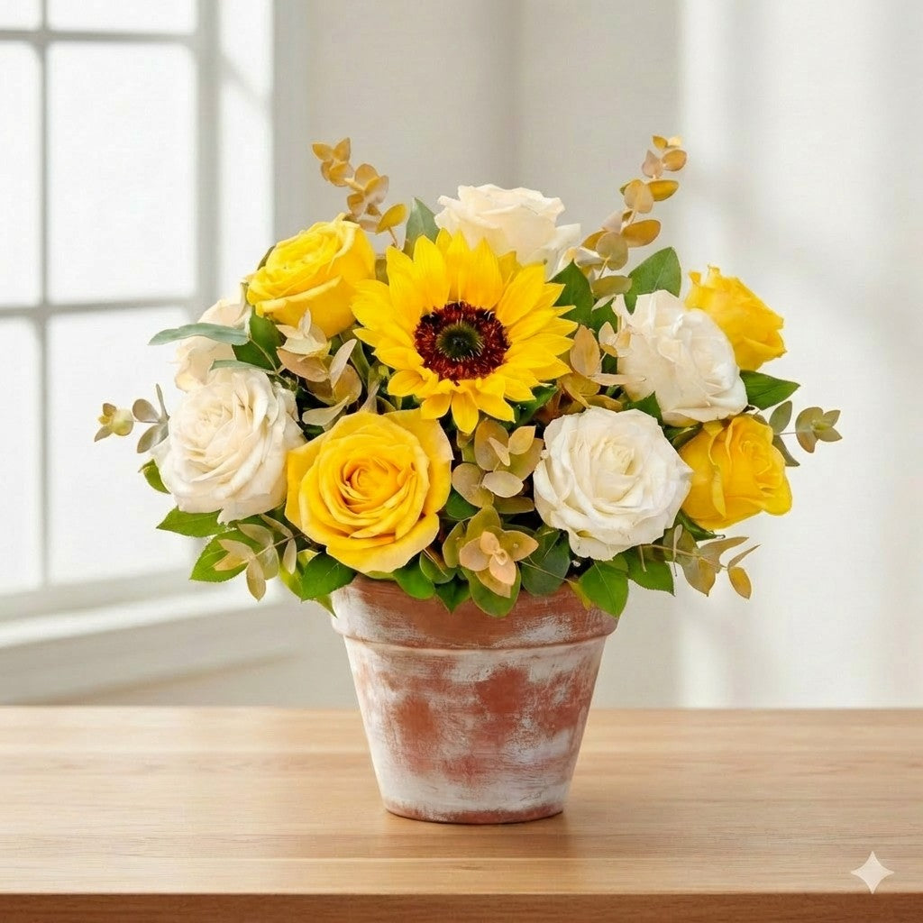 Deluxe size Radiant Grace arrangement with a sunflower, ivory and yellow roses, baby’s breath, and fuller greenery arranged in a ceramic pot – Carlsbad flower delivery.
