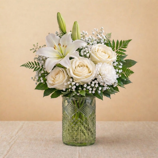 Regular size Serenity Grace white sympathy arrangement featuring white lilies, ivory roses, chrysanthemums, and soft greenery in a clear glass vase — Escondido florist.
