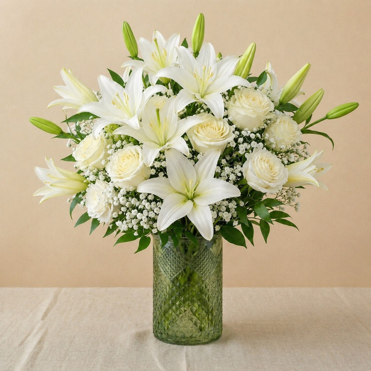 Extra full size Serenity Grace elegant white sympathy arrangement showcasing abundant white lilies, ivory roses, chrysanthemums, and lush greenery in a clear glass vase — Escondido florist.
