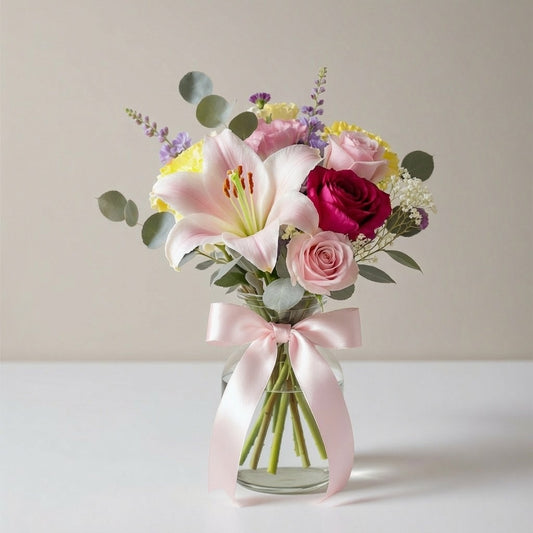 Regular size pink lily and rose bouquet with yellow accents and greenery in a clear vase with a blush ribbon — same-day flowers Escondido.