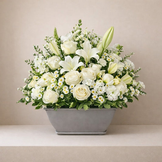 Elegant sympathy basket arrangement with white roses, lilies, and soft yellow blooms in a modern gray container - Vista florist.