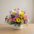 Bright mixed flower arrangement with pink roses, yellow gerbera daisies, lavender mums, and eucalyptus in a white ceramic vase – Carlsbad flower delivery