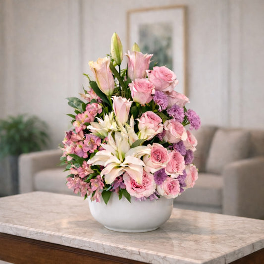 Elegant floral arrangement with blush pink roses, white lilies, pink alstroemeria, and purple accent flowers in a white ceramic bowl, handcrafted local flower delivery in Encinitas