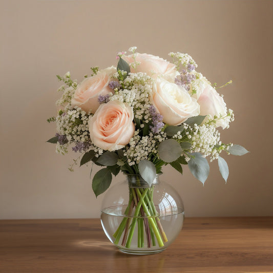 Regular size elegant vase arrangement featuring soft blush roses, white blooms, baby’s breath, and eucalyptus greenery arranged in a clear round glass vase — Carlsbad flower delivery.