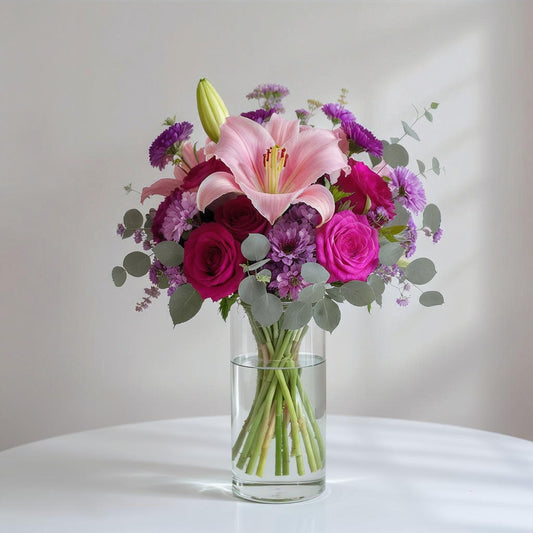 Regular size pink and purple fresh flower arrangement with lilies, roses, and mixed greenery in a clear glass vase — Oceanside flower delivery.