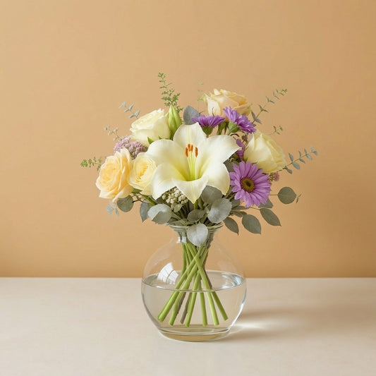 Regular size elegant white and purple bouquet featuring lilies, daisies, roses, and lush greenery in a clear round vase — Same-day flowers Vista.