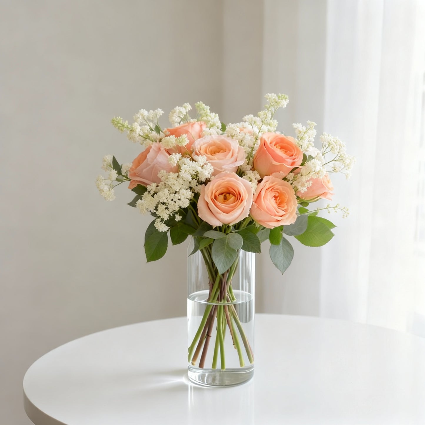 Regular size peach rose arrangement with soft peach roses, cream spray roses, astilbe, eucalyptus, and greenery in a clear glass vase on a white round table - Same-day flower delivery Oceanside.