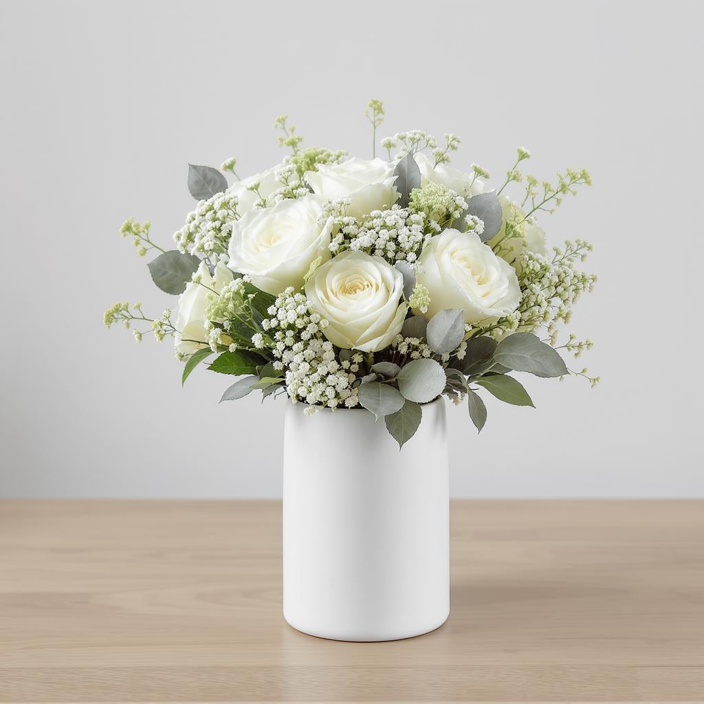 Regular size white rose arrangement with cream roses, baby’s breath, eucalyptus, and soft greenery in a tall white ceramic vase on a wooden table - Escondido flower delivery.