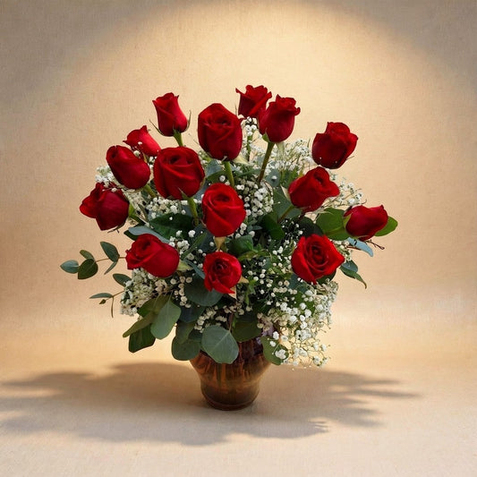 Deluxe size classic red rose arrangement with fuller long-stem red roses, enhanced baby’s breath, and lush greenery in a clear round glass vase — Vista flower delivery.