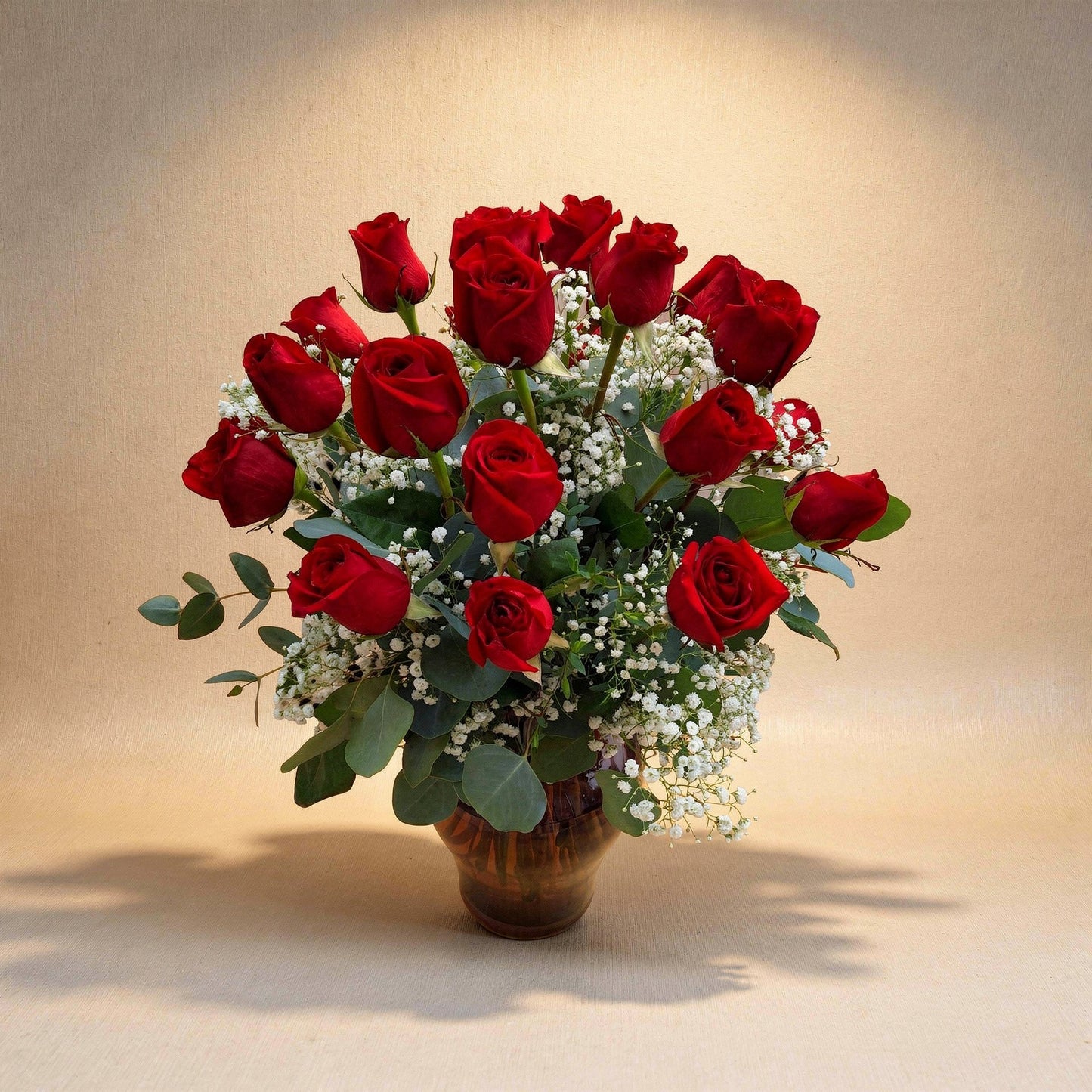 Premium size luxurious long-stem red rose arrangement with abundant roses, rich greenery, and full baby’s breath in a clear round glass vase on a white marble surface — Vista flower delivery.